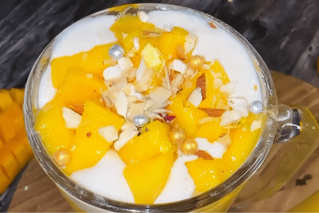 Mango Mastani garnished with mango chunks and edible silver, golden balls