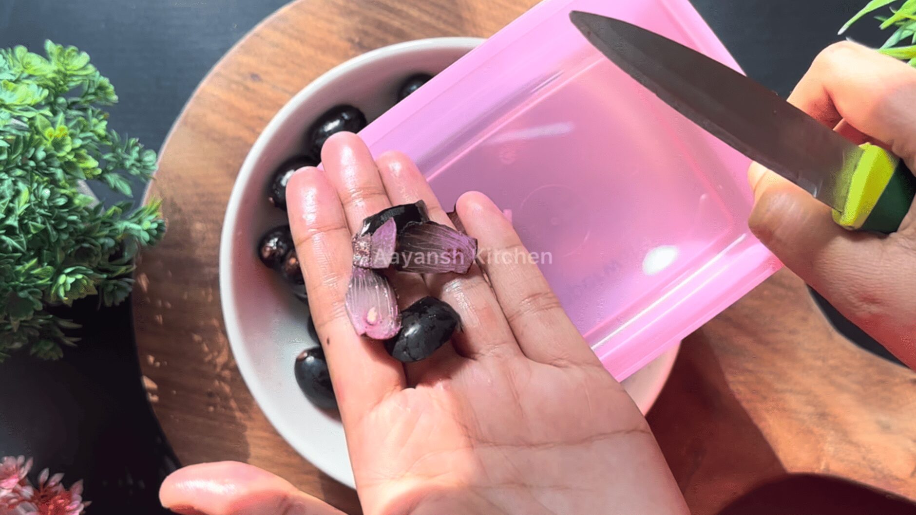 sharp knife slicing through a jamun to separate the rich purple pulp from the seed into a bowl